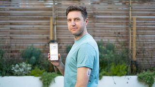 Bărbat care arată spre telefonul lui cu aplicația Dexcom și un senzor Dexcom ONE aplicat pe braț